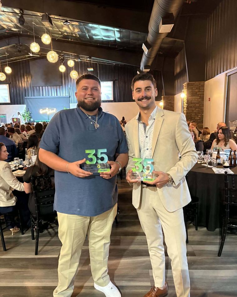 Bryndyn Lawrenz, left, holding his glass Top 35 Under 35 award beside a fellow honoree at the 2026 banquet.