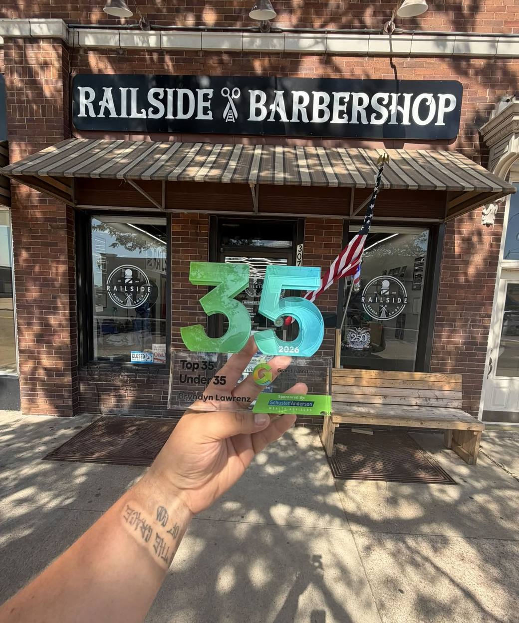 The Railside Barbershop storefront on North Walnut Street, with Bryndyn Lawrenz's Top 35 Under 35 award held up in front of the sign.