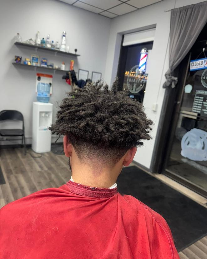 Sponge-twisted curls left full on top over a clean low taper, seen from behind under a red cape.