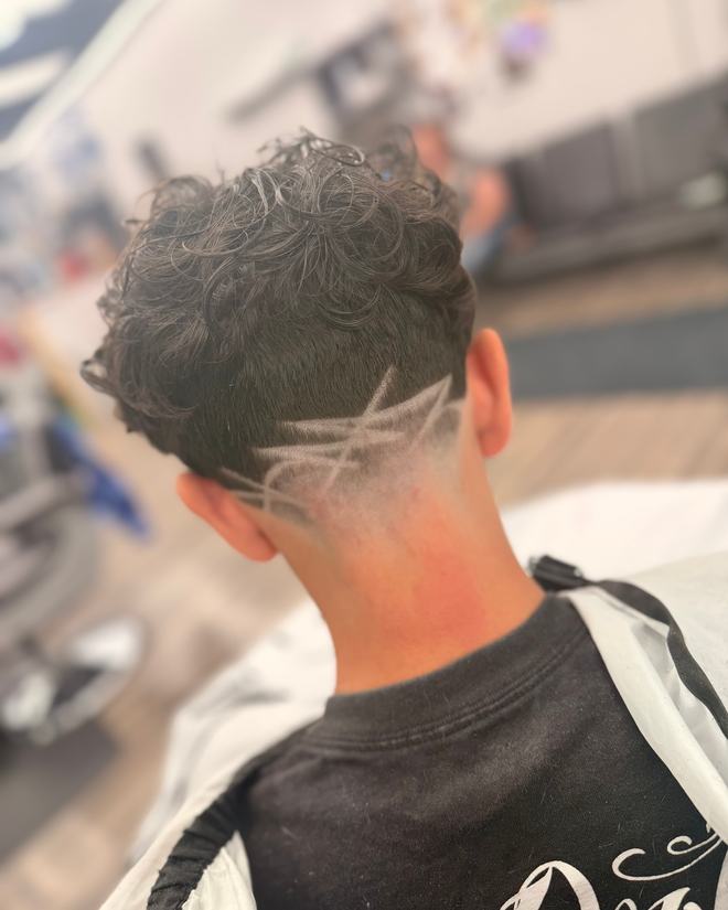 Loose curls on top over a skin fade, with a crossed-line design etched into the side.
