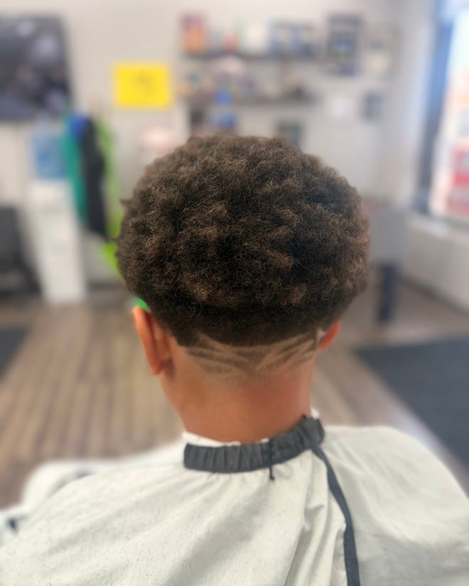 A curly top with a taper fade and a zigzag design cut in above the ear.