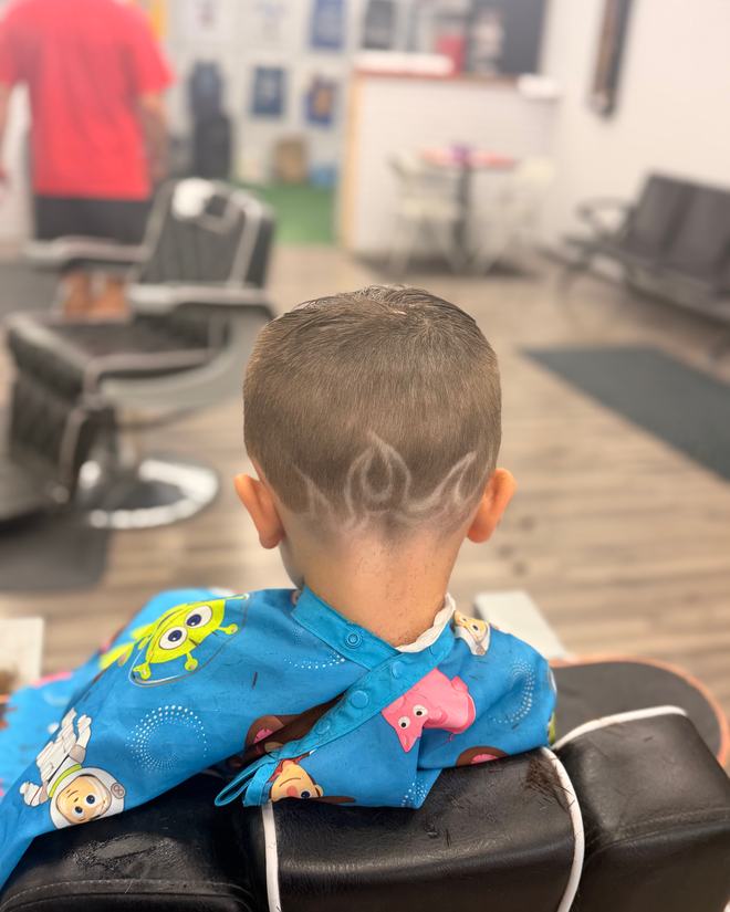 A kid's short cut with a flame design etched above the ear, in a cartoon-print cape.